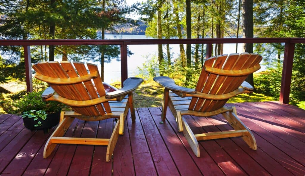 Two adirondack chairs on a deck overlooking a lake.